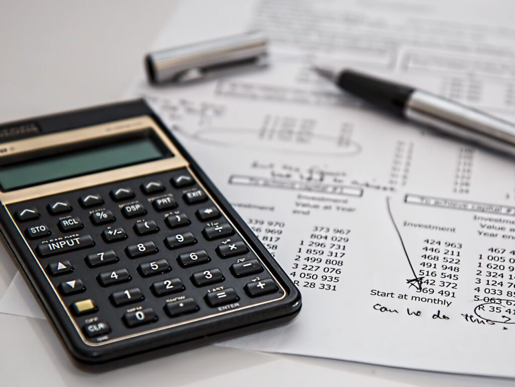 A calculator, a pen, and financial documents with printed numbers and charts are placed on a desk.