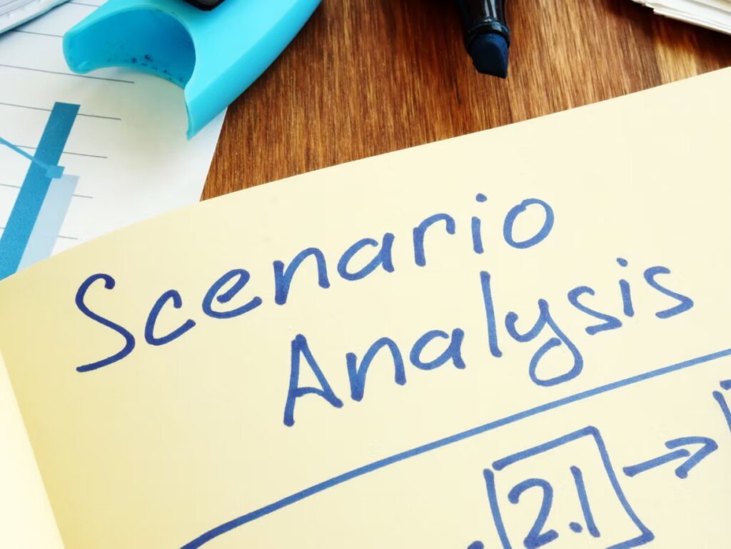 A notebook page with "Scenario Analysis" written in blue marker, next to a chart, a blue highlighter, and documents on a wooden desk.